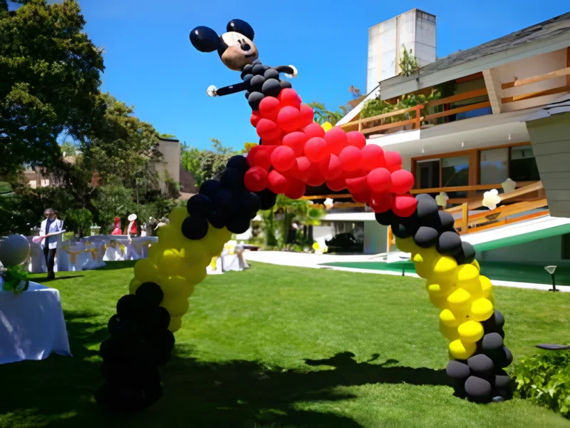 Arco de globos rojos, negros y amarillos coronado por un Mickey de globos en un jardín