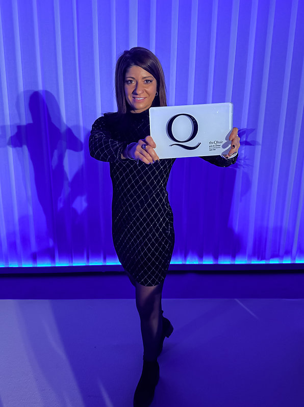 Lorena Campillo, de pie ante un fondo azul, muestra el galardón Q de Calidad de la Peluquería Española