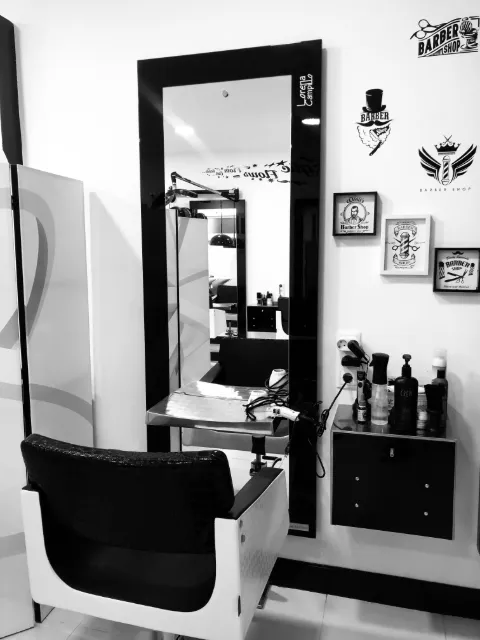 Puesto de caballero del salón: espejo de marco negro, sillón blanco y láminas de barbería en la pared