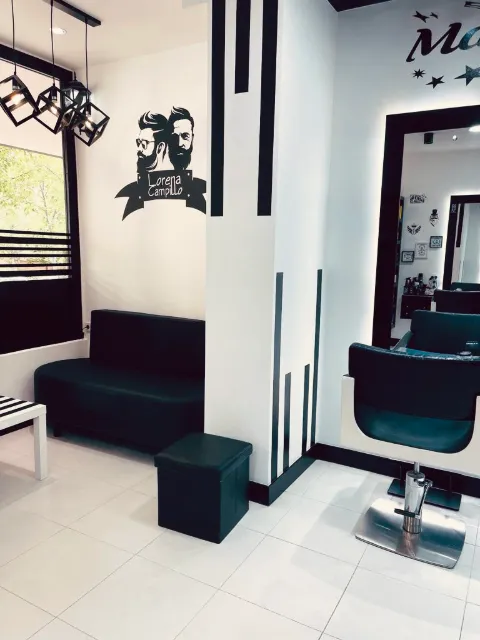 Zona de espera con sofá negro y la ilustración de barberos con el logotipo del salón
