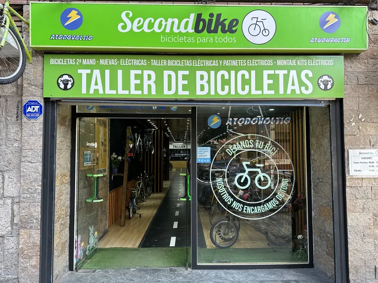 Fachada de Secondbike en la calle San Germán 70: rótulo verde «Taller de bicicletas» y puerta de cristal con el carril bici al fondo