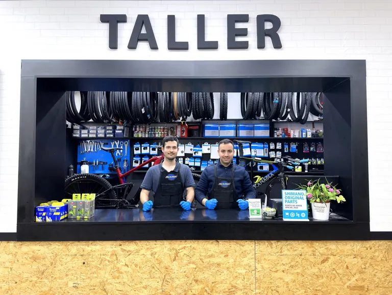 Dos mecánicos de Secondbike en el mostrador del taller, bajo el rótulo TALLER